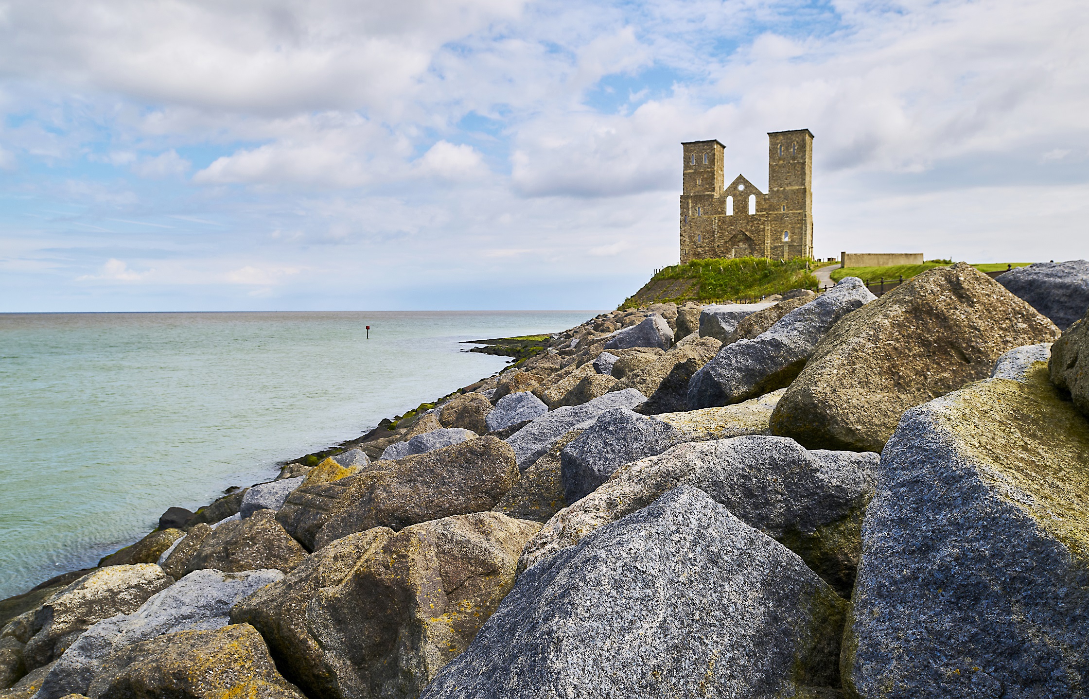 Photo of Reculver Towers and Roman Fort with rock sea defences in the foreground