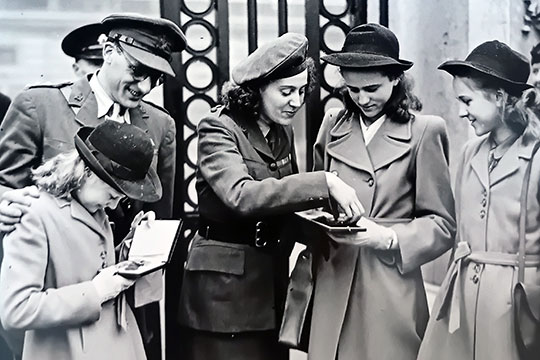 Black and white photograph of Sansom with her children, looking at her medals outside the gates of Buckingham Palace