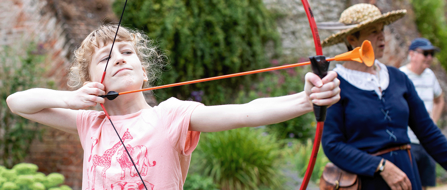 Photo of a child holding a plastic bow ready to shoot a rubber-tipped arrow as an adult watches on