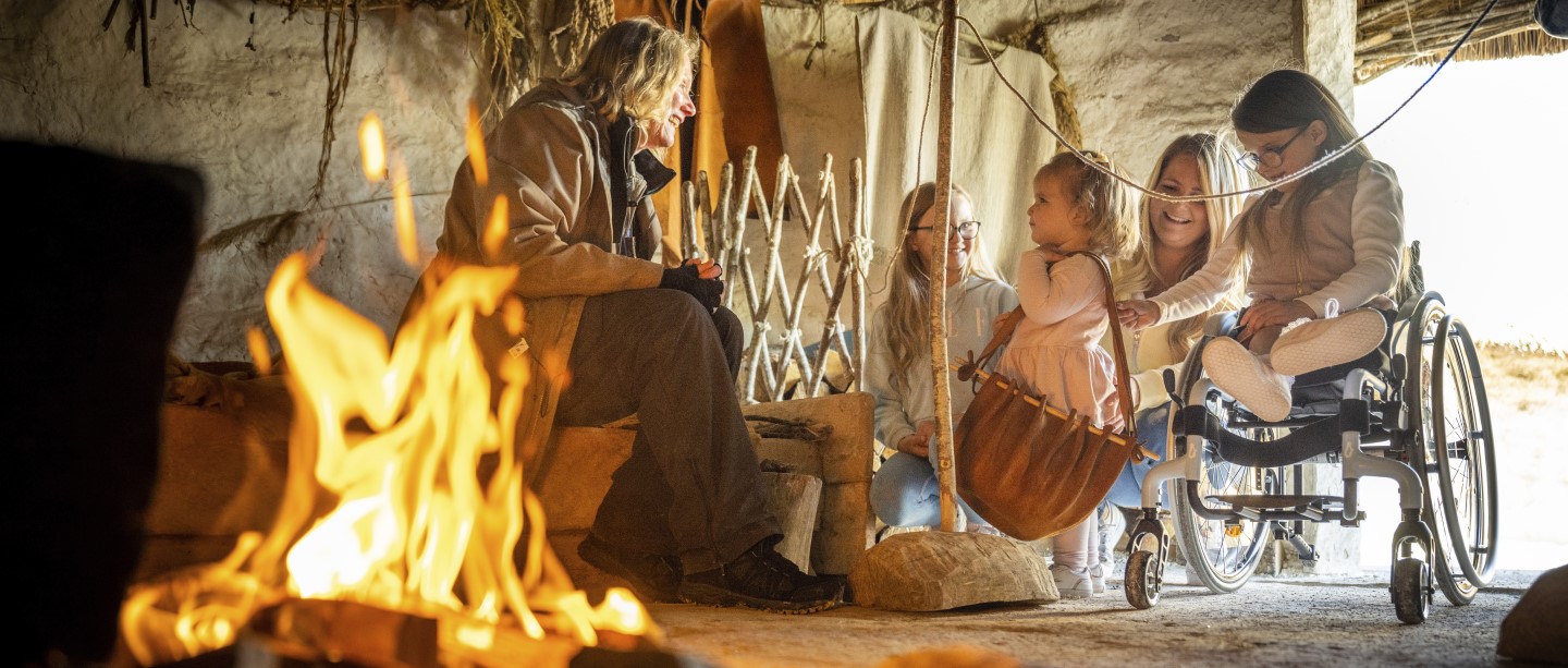 Image: Photo of people sat around a fire in a recreated Neolithic house at Stonehenge